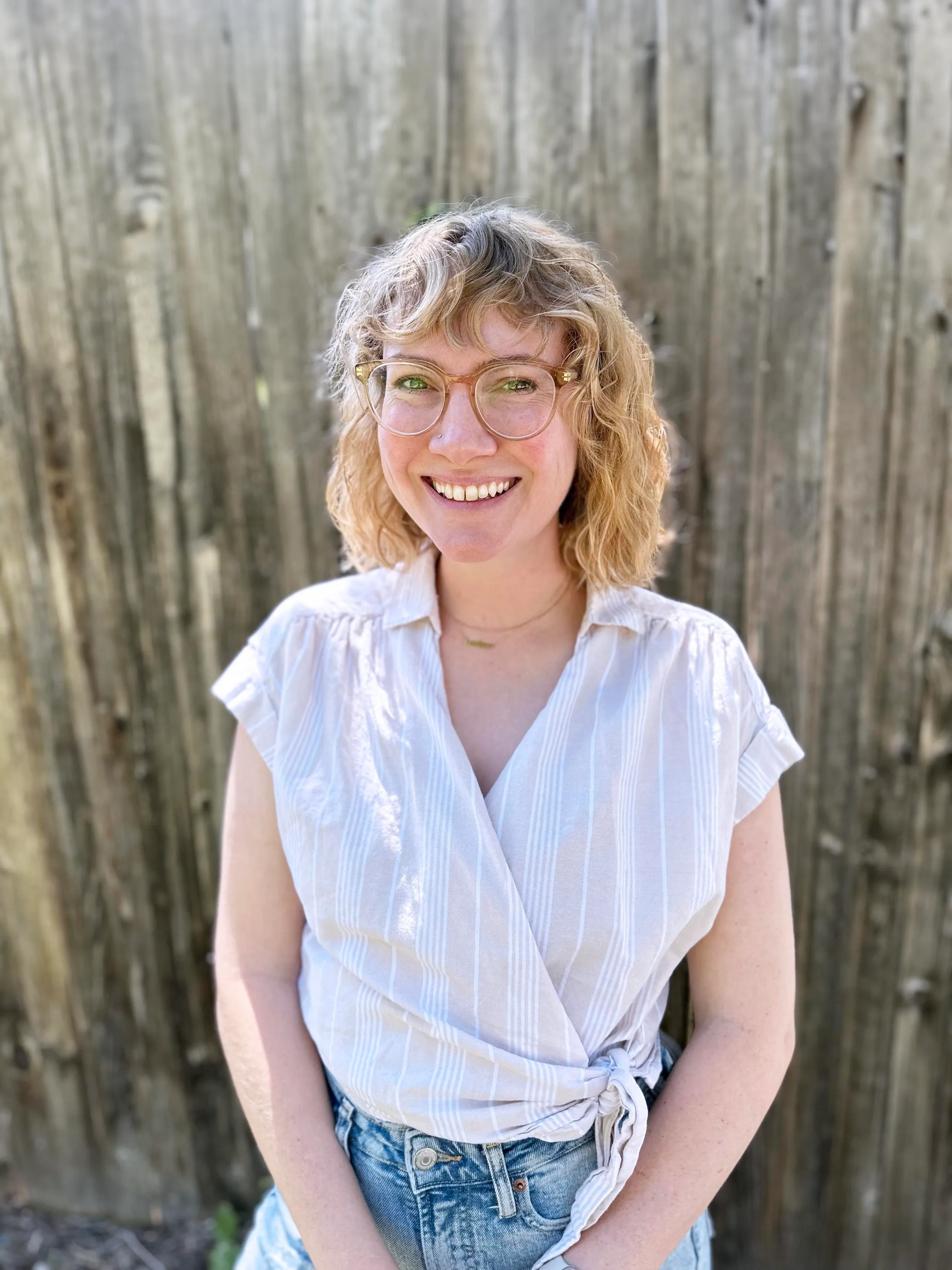 Michelle M. Taylor smiling in front of a weathered wood fence